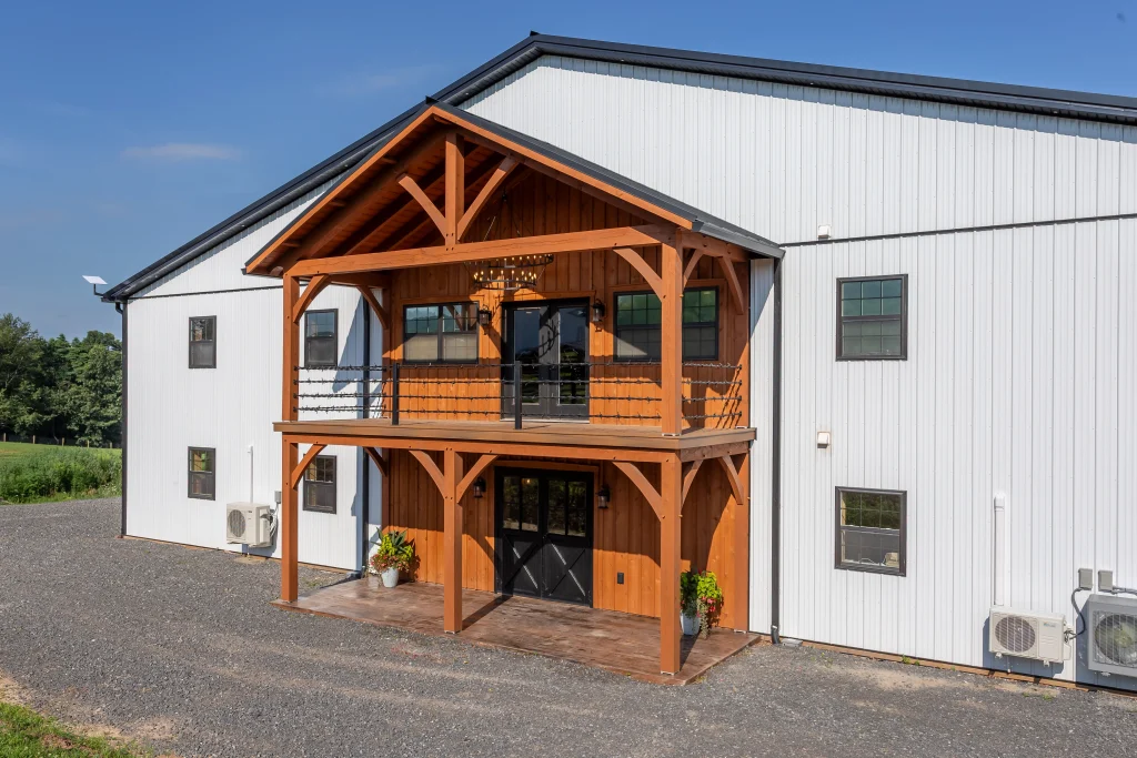 White steel-sided barn with a two-story timber-frame entry porch, upper balcony and black double doors, built by Double S Construction